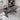 Gray desk with a laptop on a tiled floor in a room with a bookshelf.